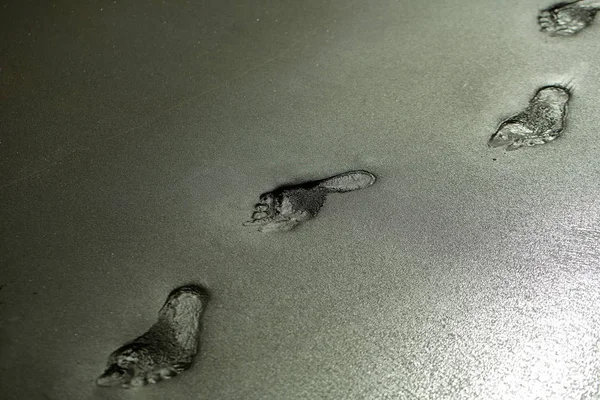 Empreintes humaines adultes ou pas de pied sur une plage de sable gris — Photo