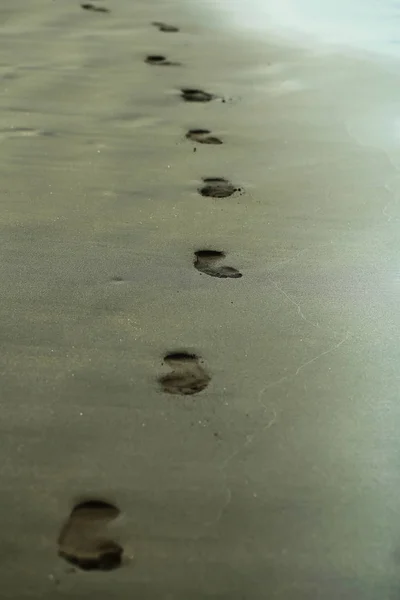 Adult human footprints or foot steps on grey sandy beach