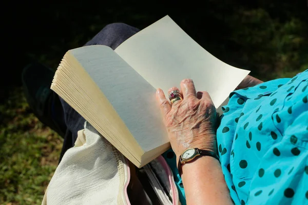 Mão feminina com pele enrugada segura livro aberto — Fotografia de Stock