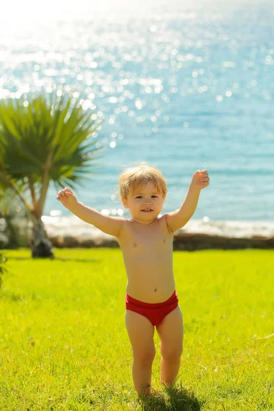 Mignon gai bébé garçon dans rouge troncs soulève les mains — Photo