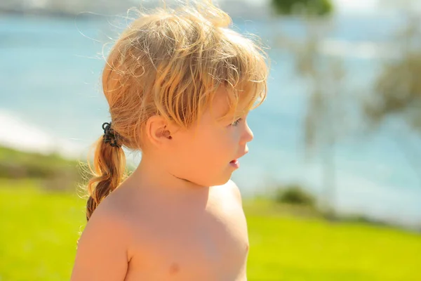 Carino bambino ragazzo con capelli biondi coda di cavallo prende il sole all'aperto — Foto Stock