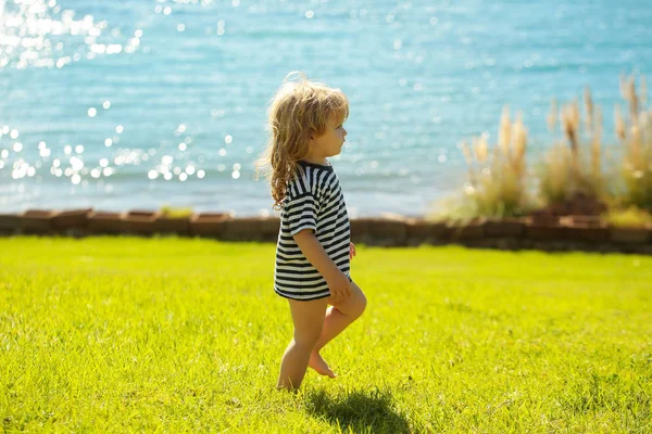 Lindo bebé niño en camiseta rayada camina sobre hierba verde —  Fotos de Stock