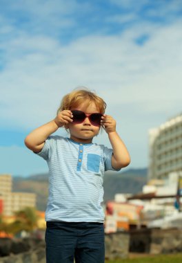 Sarışın saçlı şirin bebek çocuk moda güneş gözlüğü tutar