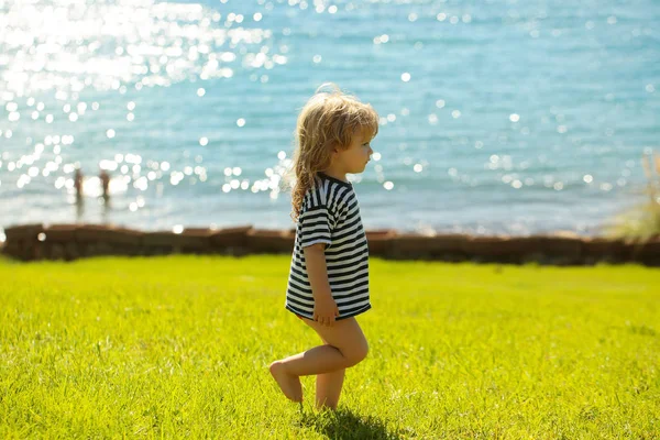 Lindo bebé niño en camiseta rayada camina sobre hierba verde —  Fotos de Stock