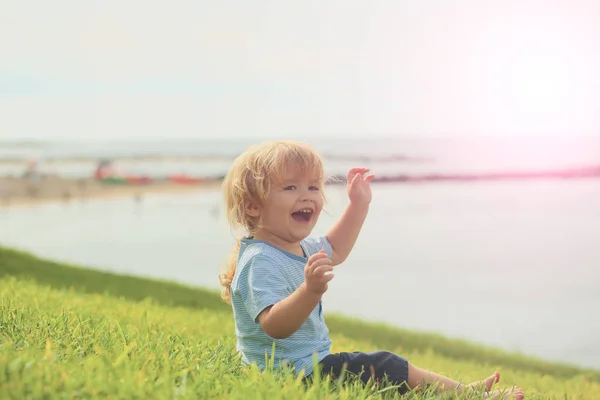 Happy cute baby boy smiles on green grass — Stock Photo, Image