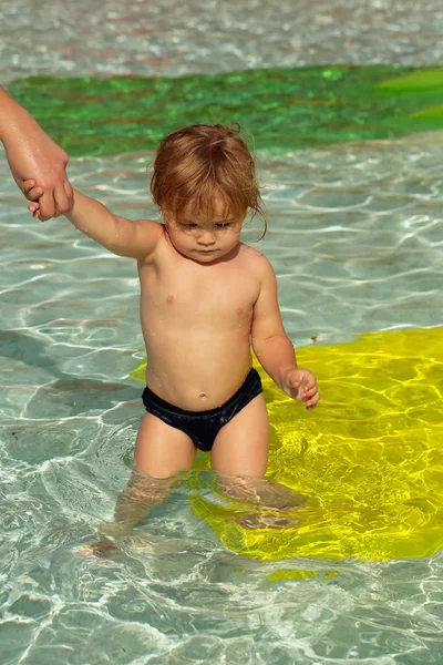 Lindo bebé niño nada en la piscina al aire libre con las madres ayudan — Foto de Stock