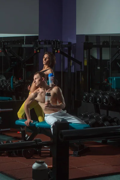 Hombre muscular y chica sexy en entrenador de gimnasio con botella — Foto de Stock