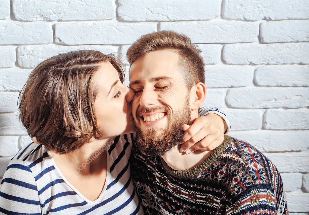 bearded man and pretty happy woman kiss on brick wall