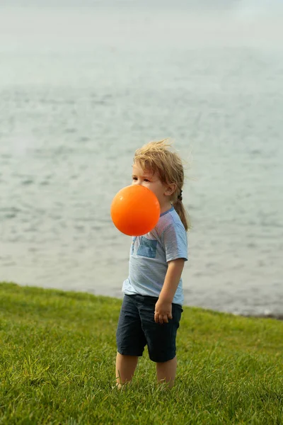 Bonito menino brinca com balão de brinquedo laranja — Fotografia de Stock