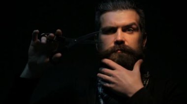 Sakallı adam makasla Sakalını kesti. Kuaför kısa sakallı kendisi yapar. Siyah arka plan çalışma keskin makas ile izole çekici yakışıklı adam 