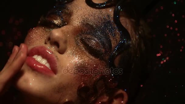 Σέξι γυναίκα αγγίζει το πρόσωπο και τα χείλη. Εντυπωσιακά δημιουργικό μακιγιάζ και το χτένισμα με χρυσό glitter για κόμμα ή μόδα εμφάνιση. Εσωτερικη seductively εξετάζοντας τη φωτογραφική μηχανή με λάμψη αίγλη μακιγιάζ κορίτσι — Αρχείο Βίντεο