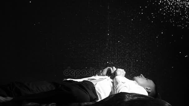 Mężczyzna leży na łóżku i guziki białą koszulę na tle czarnej ścianie w nocy. Samotność, depresja, zmęczenie i brak motywacji. Młody człowiek marzy w łóżku przed pracą — Wideo stockowe