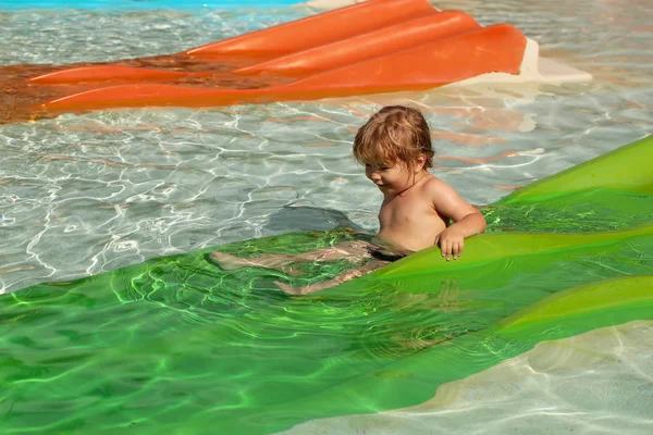 Счастливый милый мальчик скользит с зеленой водяной горки — стоковое фото