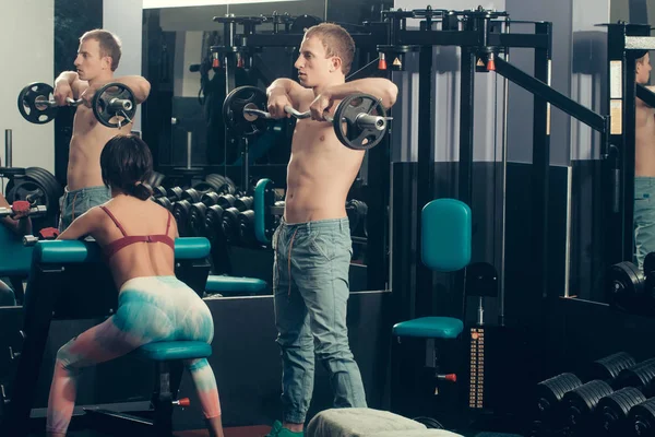 Musculoso homem e menina no ginásio com halteres e barra — Fotografia de Stock