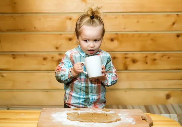 Cute child cooking with dough, flour and cup on wood — Stock Photo, Image