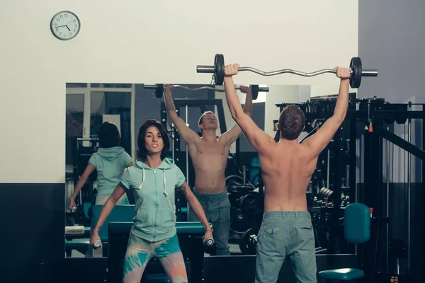 Musculoso homem e menina no ginásio com barbell e halteres — Fotografia de Stock