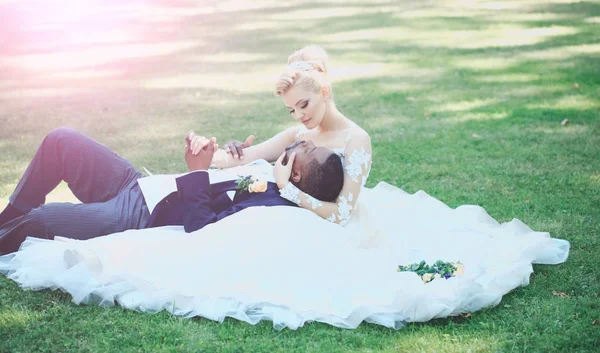 Muž leží v náručí roztomilý nevěsta na zelené trávě — Stock fotografie