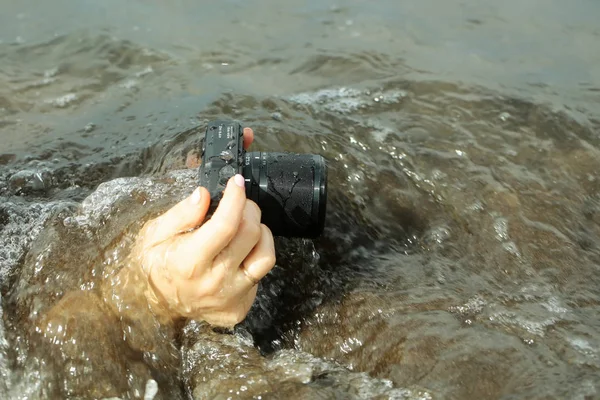 Black wet camera with lens in hands filming under sea