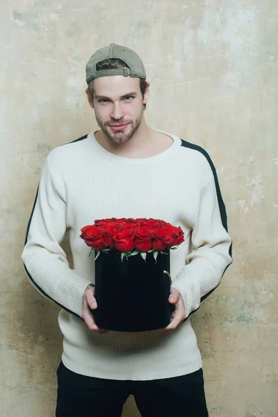 Brodaty mężczyzna uśmiechający się posiada czerwone pole Róża na teksturą ściany — Zdjęcie stockowe
