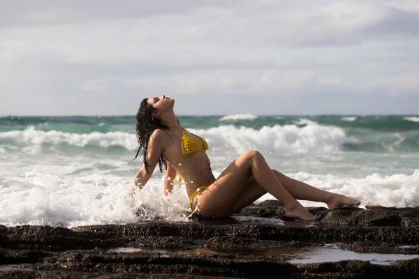Menina bonita em maiô amarelo sexy sentado na praia rochosa — Fotografia de Stock