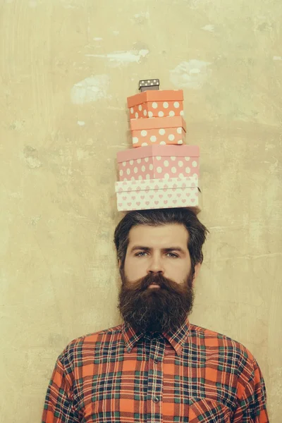 Homme barbu sérieux tenant des boîtes-cadeaux colorées empilées sur la tête — Photo