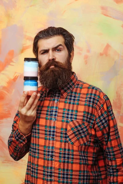 Hombre barbudo serio sosteniendo dos frascos cosméticos — Foto de Stock