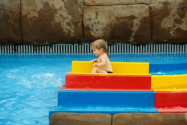 Schattige babyjongen glijden van kleurrijke glijbaan in blauw water — Stockfoto