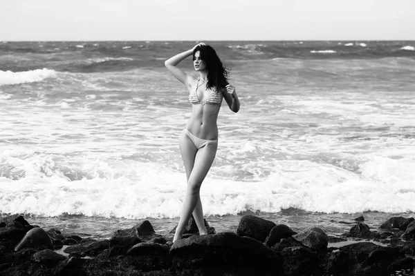 Pretty girl in sexi swimsuit standing on rocky beach — Stock Photo, Image