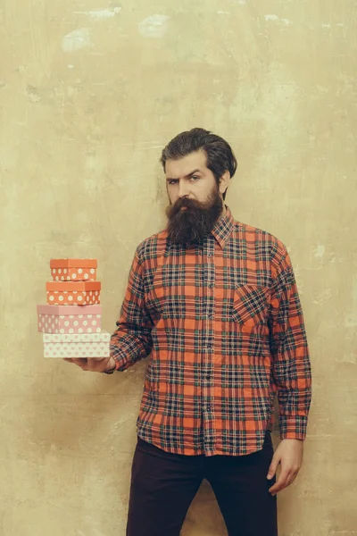 Серьёзный бородатый мужчина держит в руках разноцветные подарочные коробки. — стоковое фото