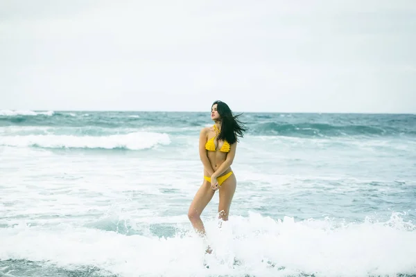 Hübsches Mädchen im sexi gelben Badeanzug steht auf einem Felsen — Stockfoto