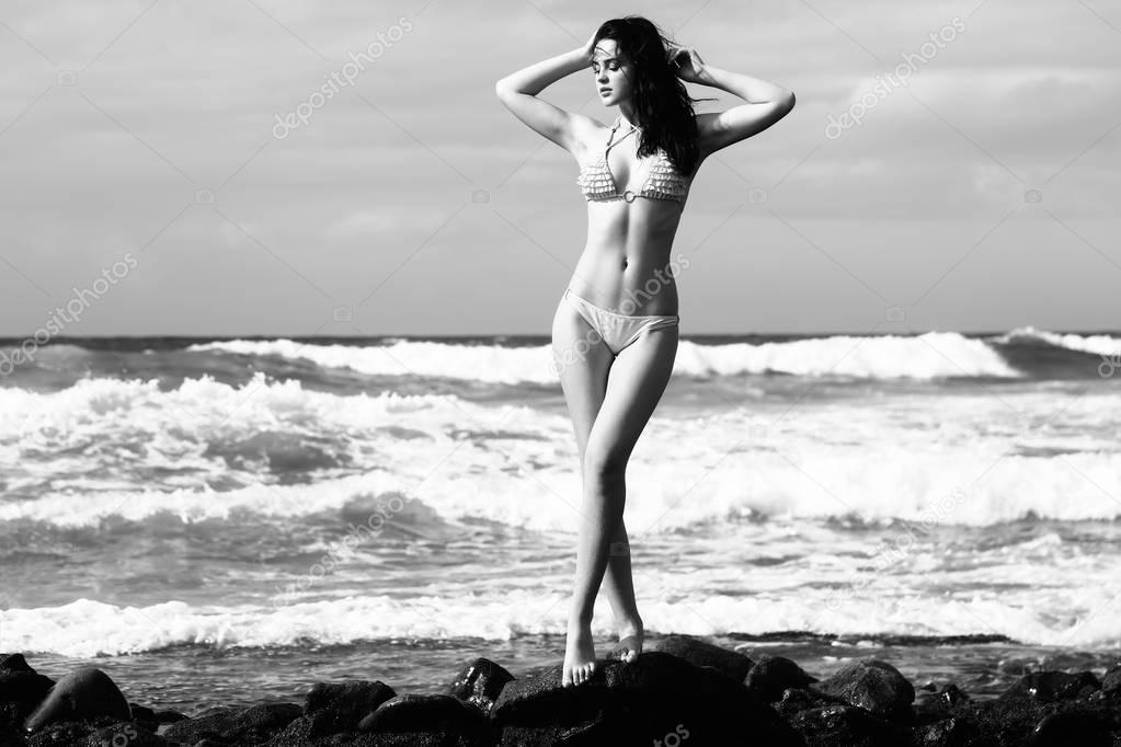 Pretty girl in sexi swimsuit standing on rocky beach