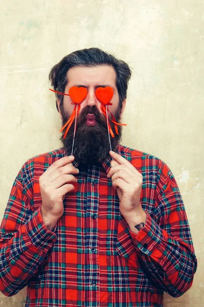 Divertente uomo barbuto che tiene i cuori rossi sui bastoni davanti agli occhi — Foto Stock