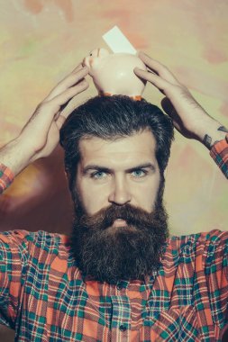 Sakallı adam kafasına pembe seramik kumbara tutan kaşlarını