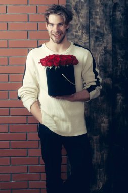 Sakallı gülümseyen adam kırmızı gül çiçekler kutusunda tutar.