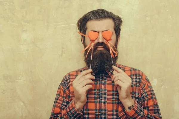 Bearded man holding red hearts on sticks before eyes — Stock Photo, Image