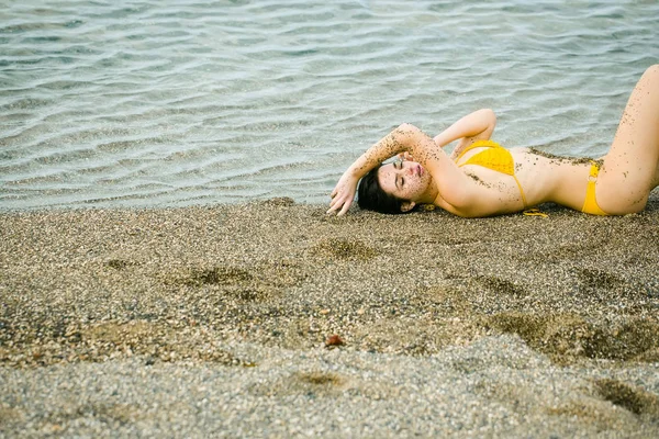 Söt flicka i gul baddräkt sovande på stranden — Stockfoto