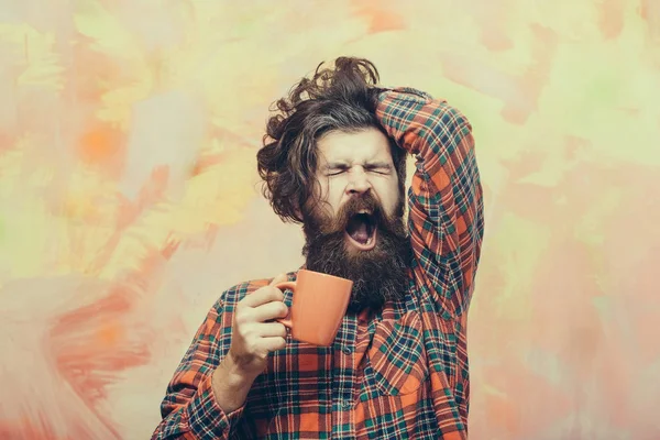 Зевущий бородатый мужчина с бахромой и оранжевой чашкой — стоковое фото