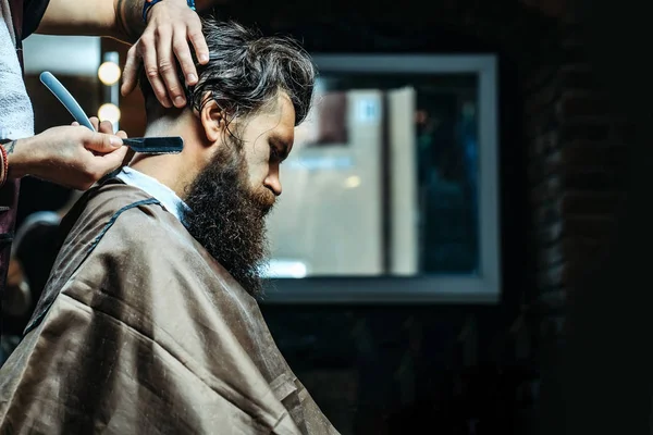 Bearded man with long beard getting hair shaving with razor