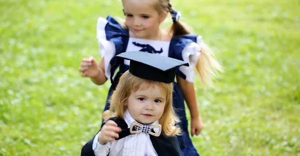Menina bonito vestir menino pequeno em chapéu de graduação e roupão — Fotografia de Stock