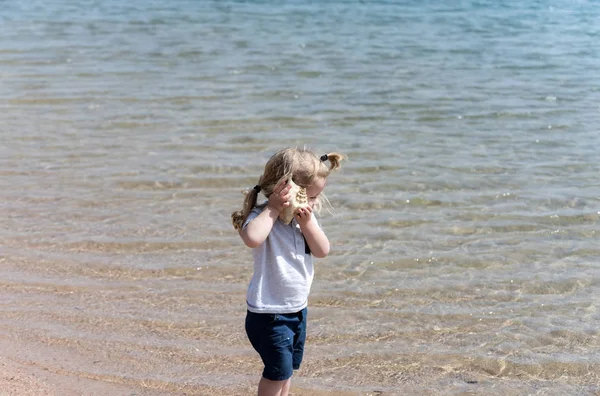 Lindo bebé niño escuchando concha marina en la playa del mar —  Fotos de Stock