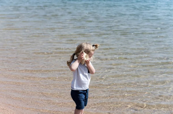 Cute baby boy listening to seashell on sea beach — Stock Photo, Image