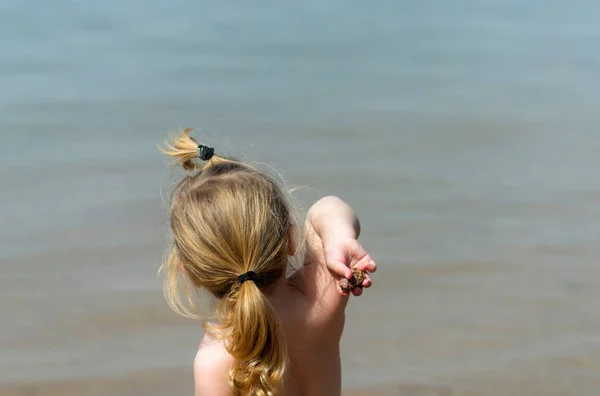 Lindo bebé niño o niña lanzando piedras en el mar azul — Foto de Stock