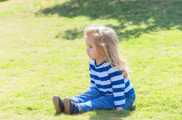 Söt glad pojke som sitter på gräset i parken — Stockfoto