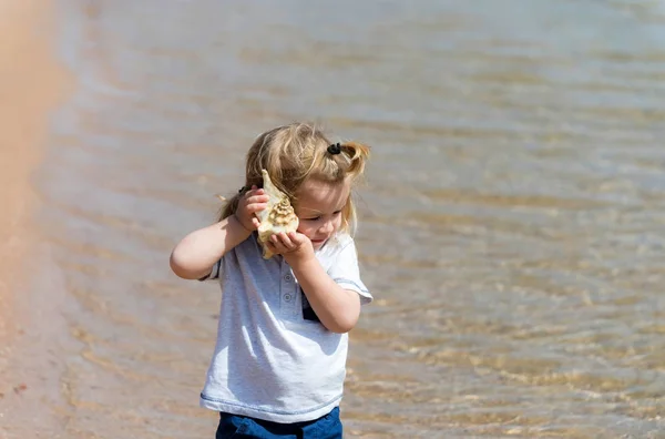 Ładny chłopczyk słuchanie muszla na plaży — Zdjęcie stockowe