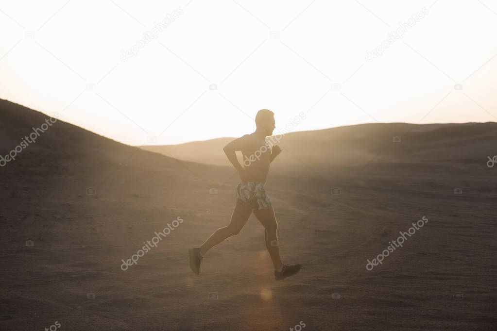 Man runner running in dune at sunset