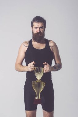 Sakallı ciddi adam gri arka plan üzerinde altın şampiyon Kupası tutar