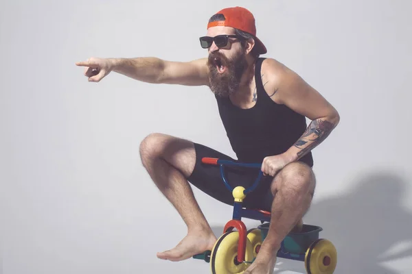 Bearded shouting man on colorful bicycle toy in sunglasses, cap — Stock Photo, Image