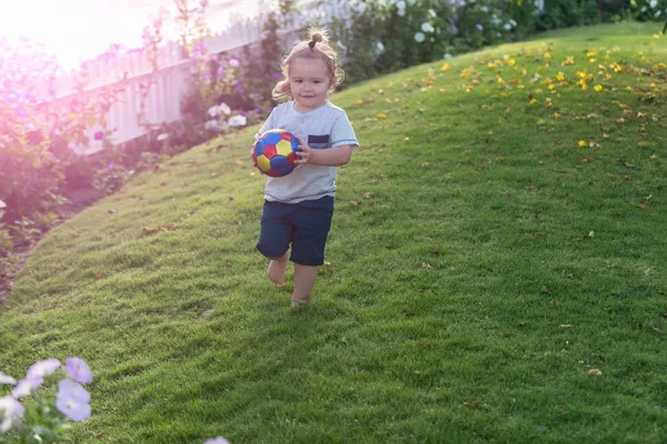 Feliz menino bonito jogando com bola na grama verde — Fotografia de Stock