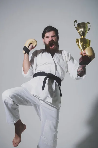 Bearded happy karate man in kimono, boxing gloves, champion cup — Stock Photo, Image