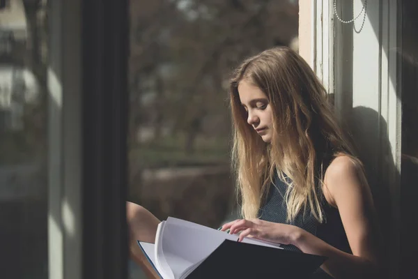 Mooi meisje leesboek op open venster — Stockfoto